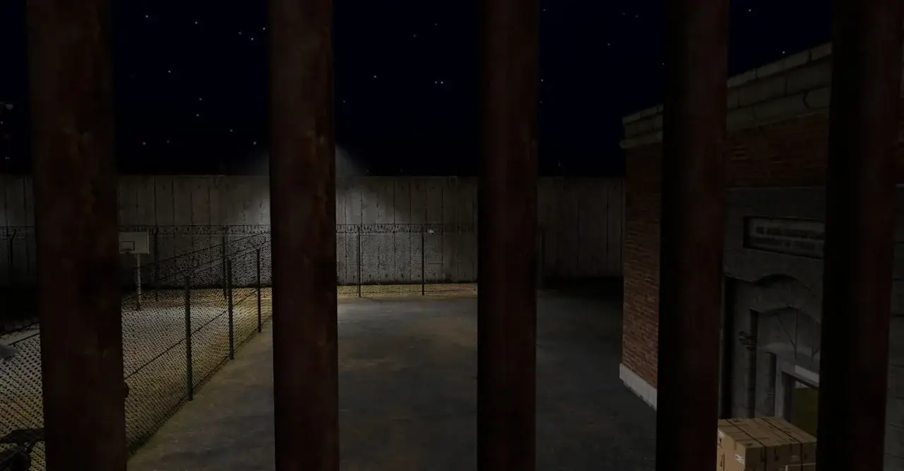 Night-time prison yard with barbed-wire fence, seen through bars