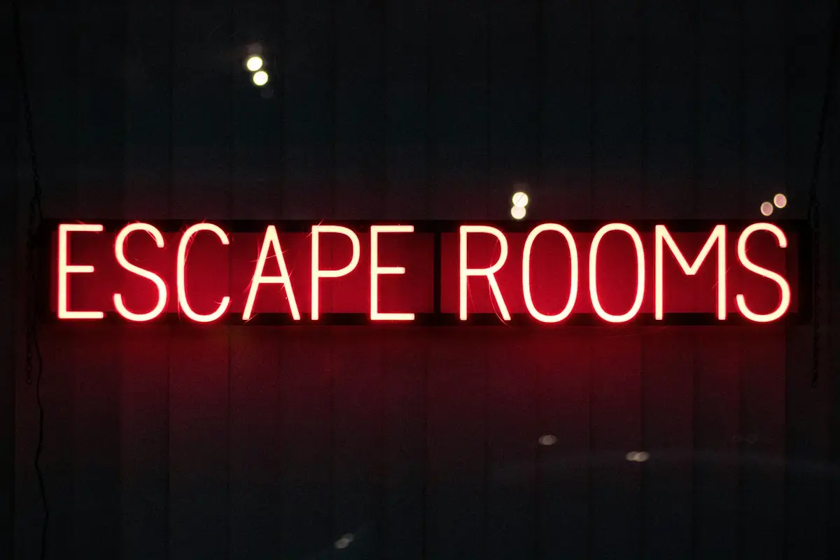 Rote Neonreklame mit der Aufschrift „ESCAPE ROOMS“ an einer dunklen Wand.