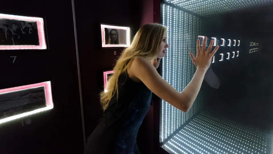 A player presses her hand against a glowing mirror tunnel in Psychosis, with lit photos on the wall beside it